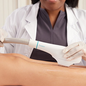 Medical professional wearing gloves using a handheld device on a patient's leg during a treatment.
