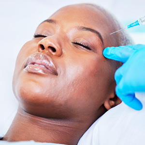 Close-up of a woman receiving a cosmetic injection near her temple from a gloved professional.