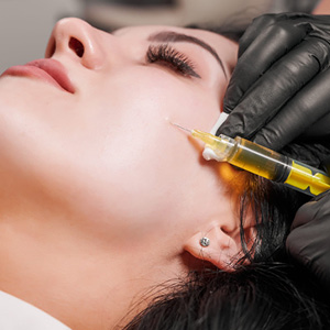 Close-up of a woman receiving a cosmetic injection in her cheek administered by a gloved hand.