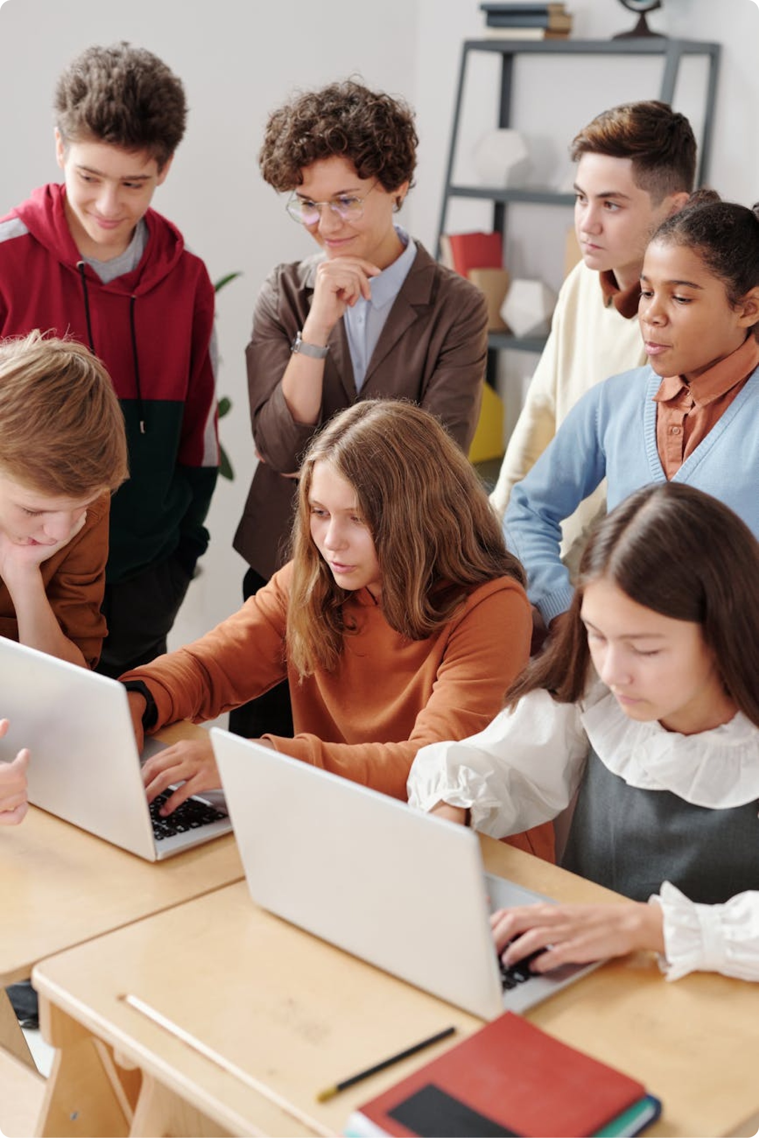 A teacher and six students collaborating around two laptops in a classroom.