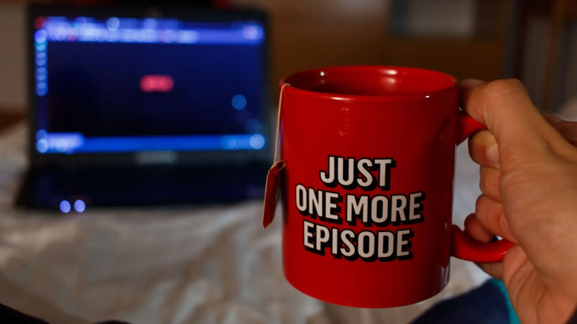 A person holds a red coffee cup that reads "Just One More Episode" while watching Netflix