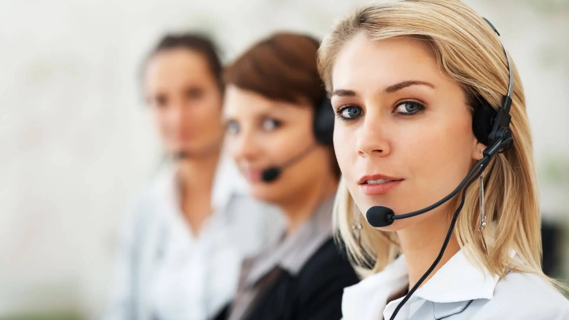 A blonde, customer service woman with a microphone looks at the camera in a customer service center.