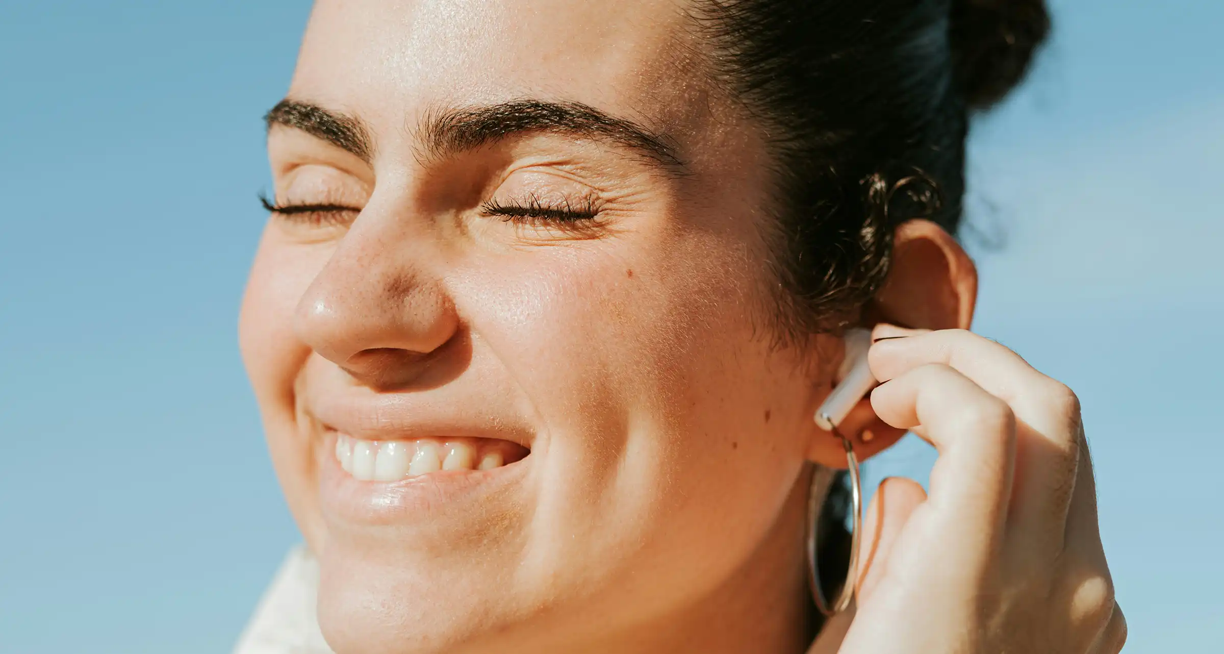 Woman with radiant, youthful skin smiling in the sun, showcasing a glowing complexion and natural beauty.