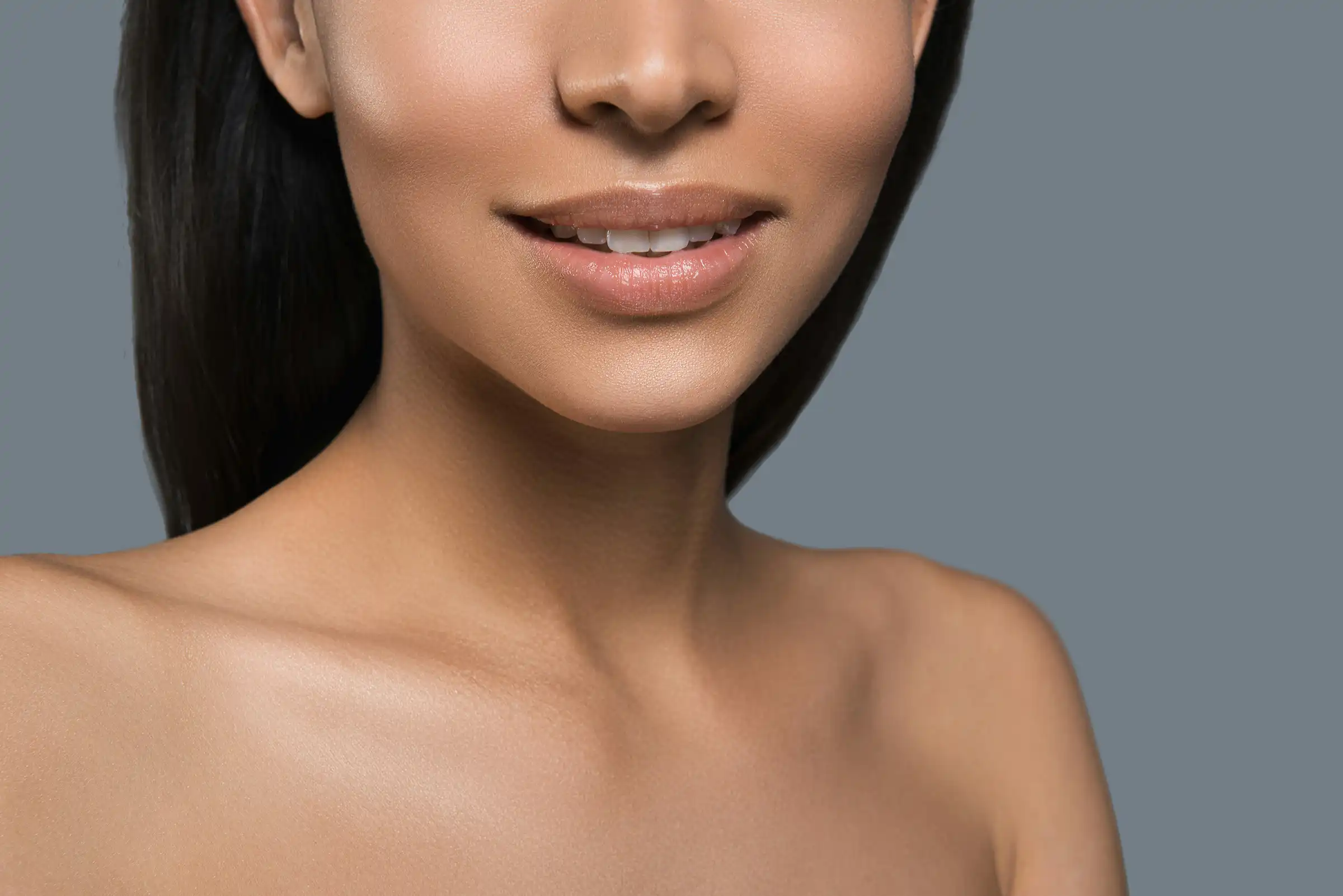 Close-up of a woman’s lower face, lips, and décolletage with smooth, even-toned skin and a soft smile, emphasizing radiant complexion and natural beauty.