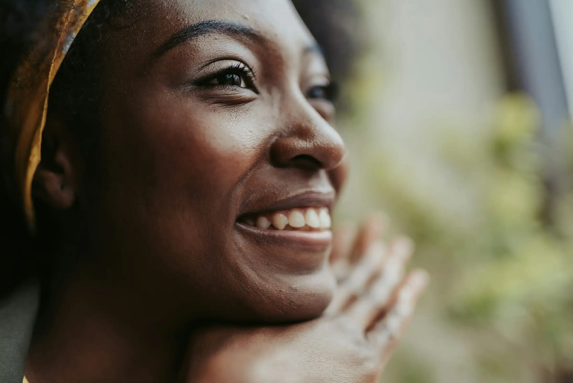 Close-up of a joyful woman resting her chin on her hands, showcasing smooth, glowing skin and a confident smile in soft natural light.