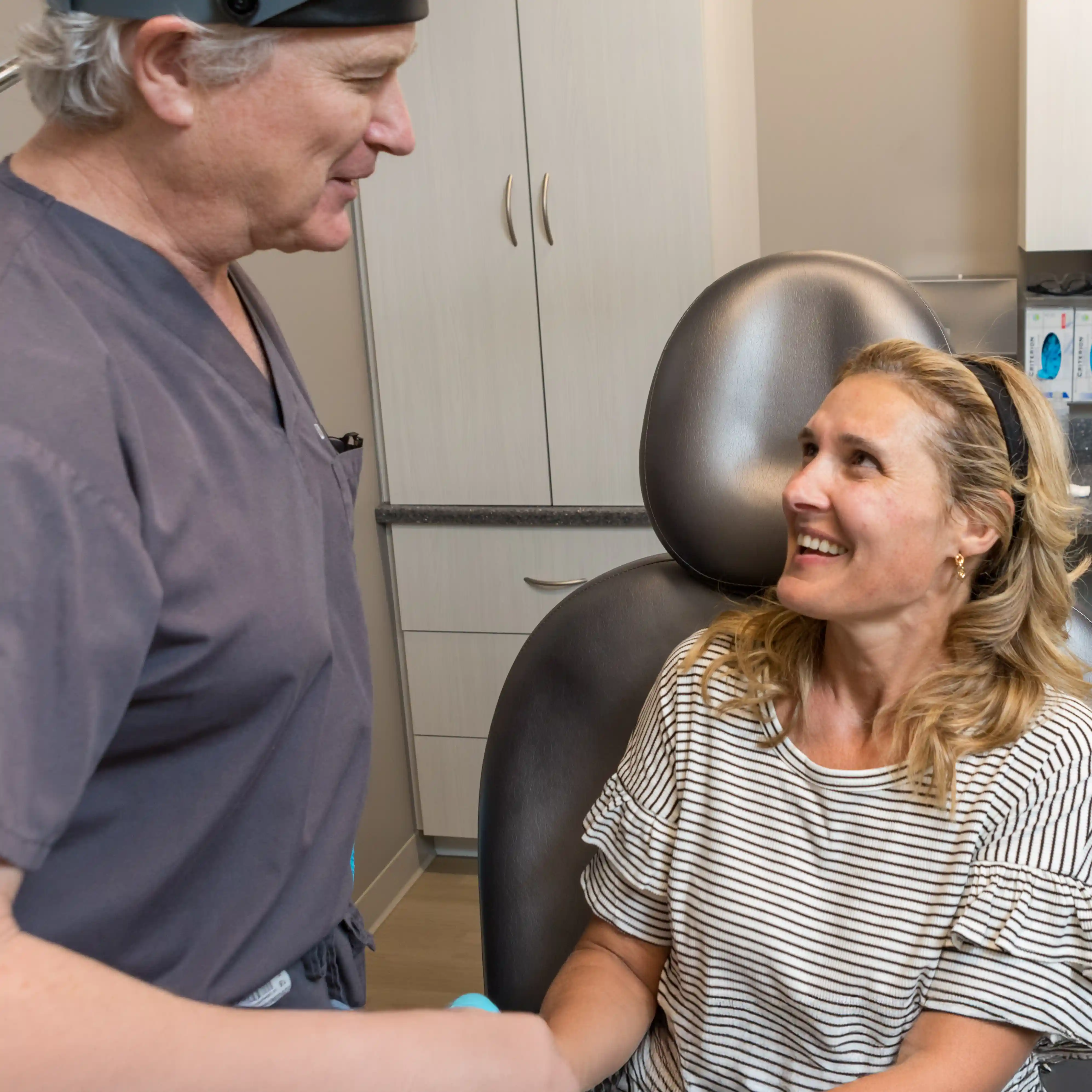 Dr. LaBine smiling and speaking with a patient in a dermatology exam room, highlighting compassionate, personalized care and skin health expertise.