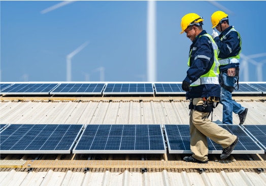 Two electricians walking on the roof of a large industrial building, checking the solar panels they installed. 