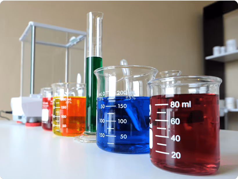 A row of laboratory glassware containing colorful chemical solutions, including red, blue, green, and yellow liquids.