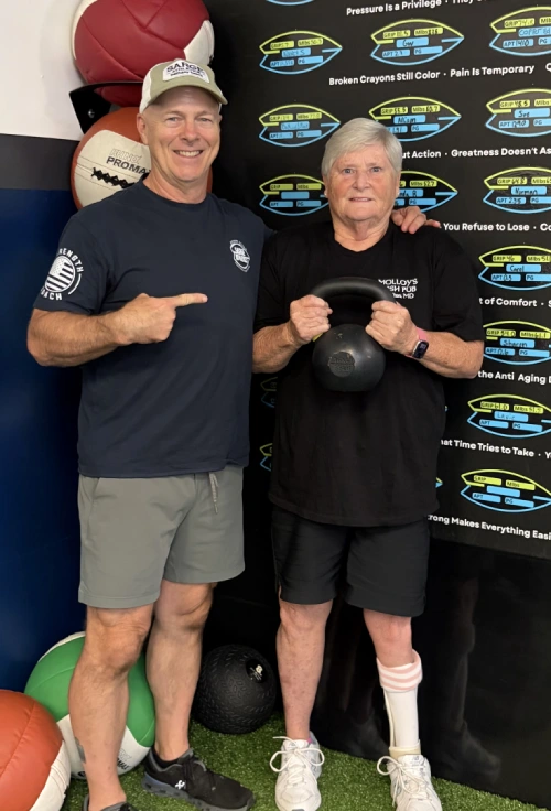 Fitness coach posing with a client holding a kettlebell in a gym.