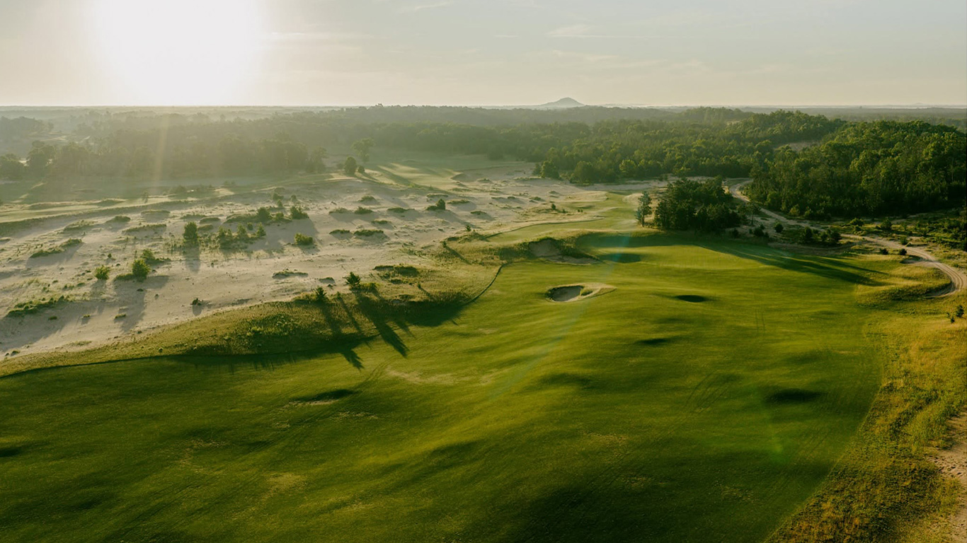 Aerial view of a Sand Valley Golf Resort course at sunrise, showing dunes and a green with bunkers