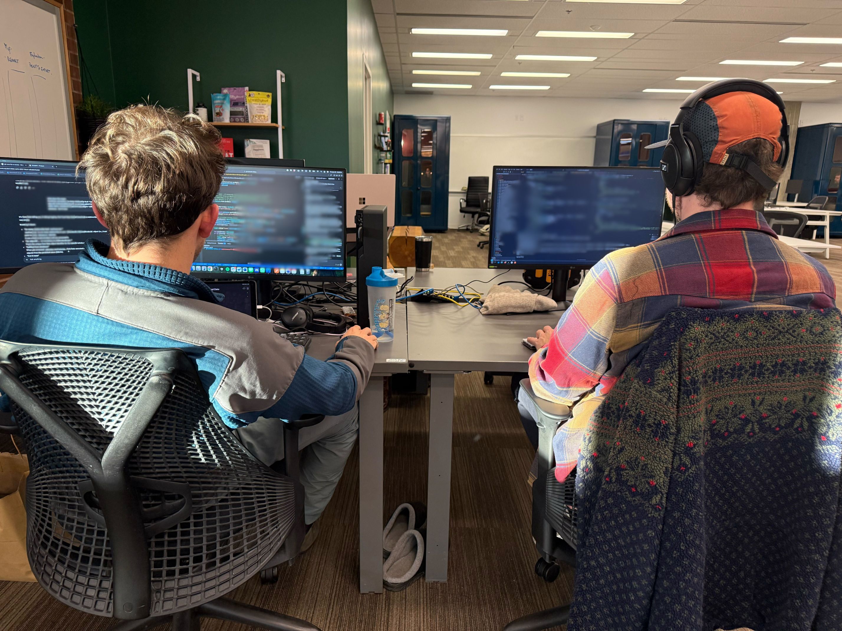 Two software engineers working at desks with multiple monitors displaying code in a modern office.