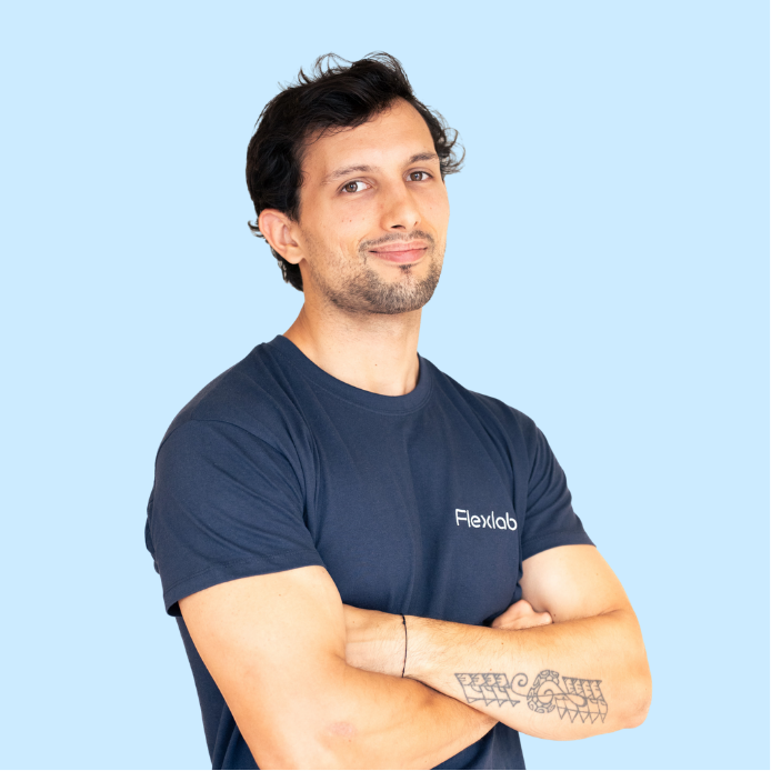 Portrait d’un flexologue de l’équipe Flexlab, debout en position confiante, mains sur les hanches, portant le t-shirt bleu marine officiel du studio. L’image reflète l’approche professionnelle, positive et dynamique du stretching assisté chez Flexlab.