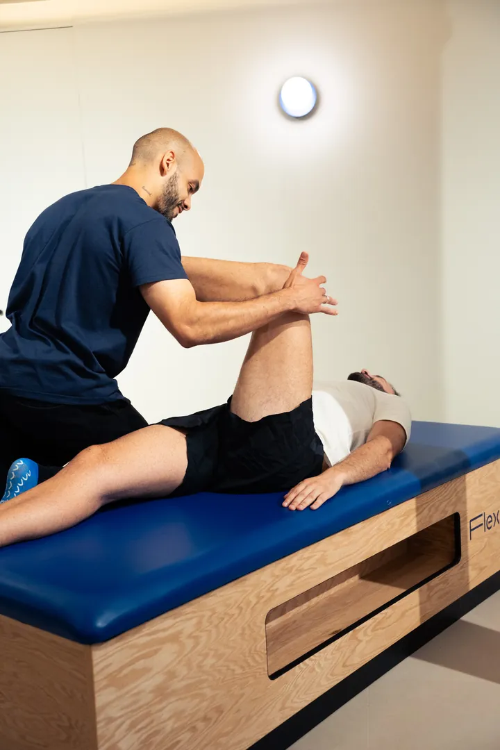 Une femme effectue une posture de yoga dans un espace lumineux, les bras tendus en arrière et une jambe fléchie en avant. Elle porte un ensemble de yoga beige et semble concentrée tout en pratiquant une posture d’étirement.