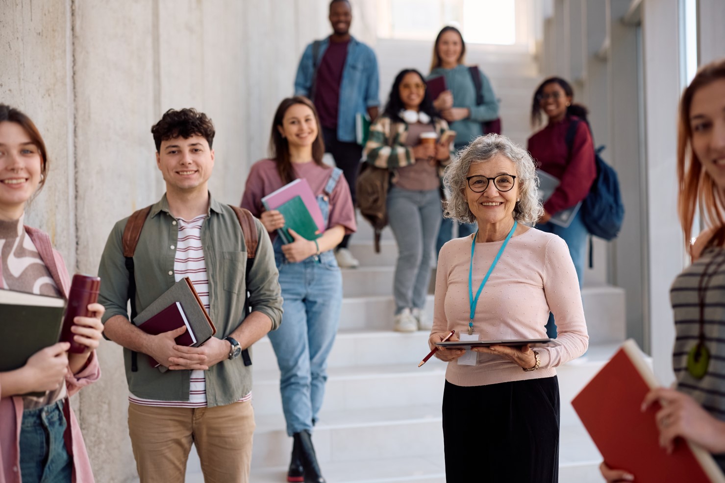 Grupa studentów z wykładowcą stojących na schodach w budynku szkoły wyższej.