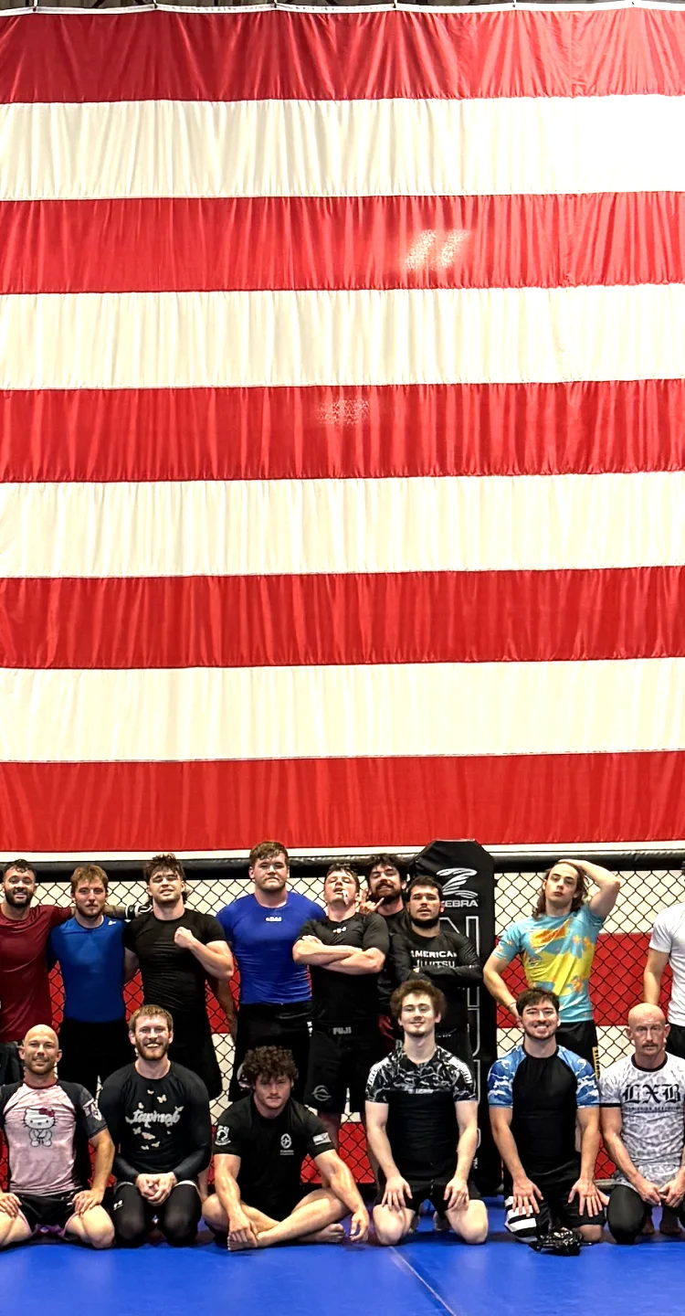American Jujitsu team members posing together in front of a large American flag inside the gym in Springfield, IL