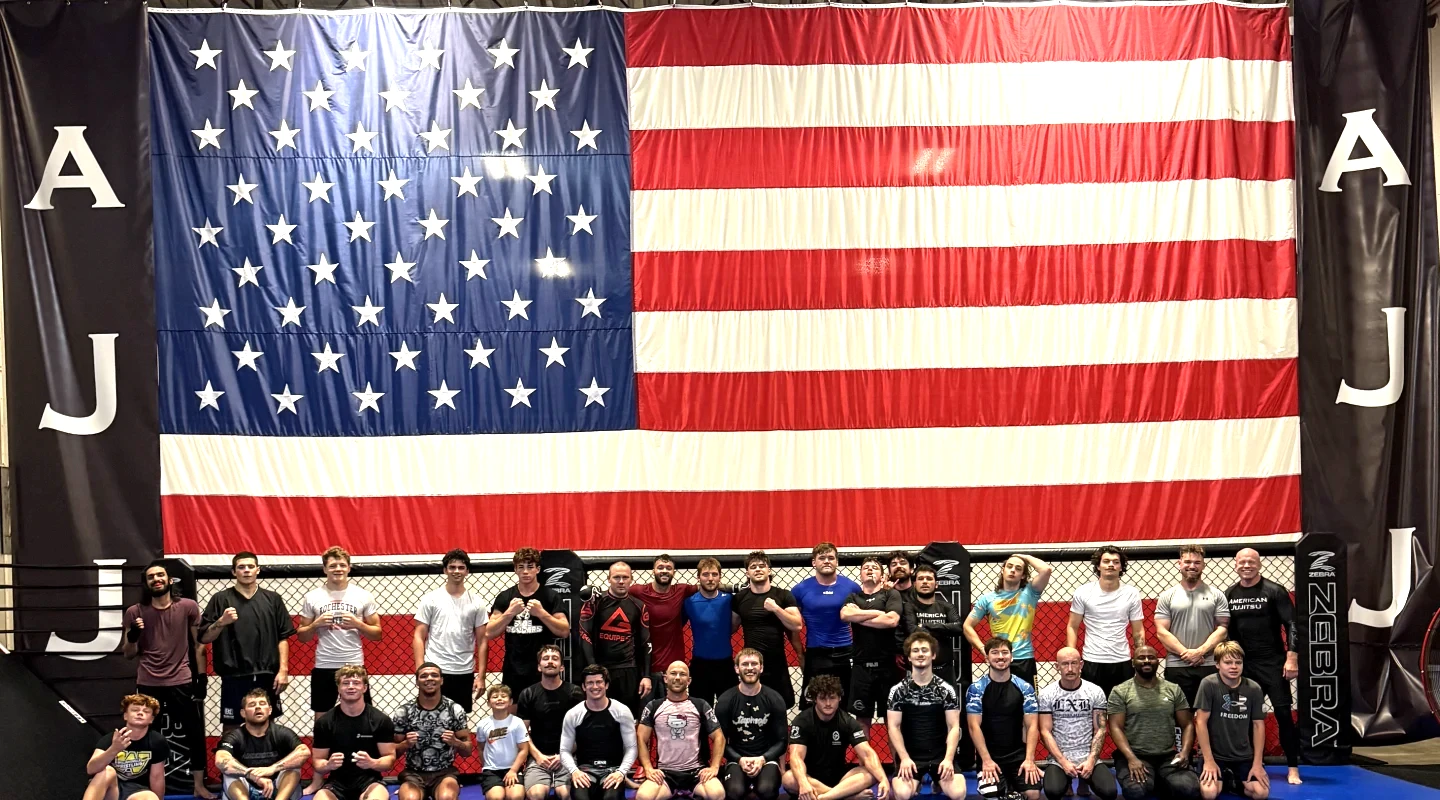 American Jujitsu team members posing together in front of a large American flag inside the gym in Springfield, IL