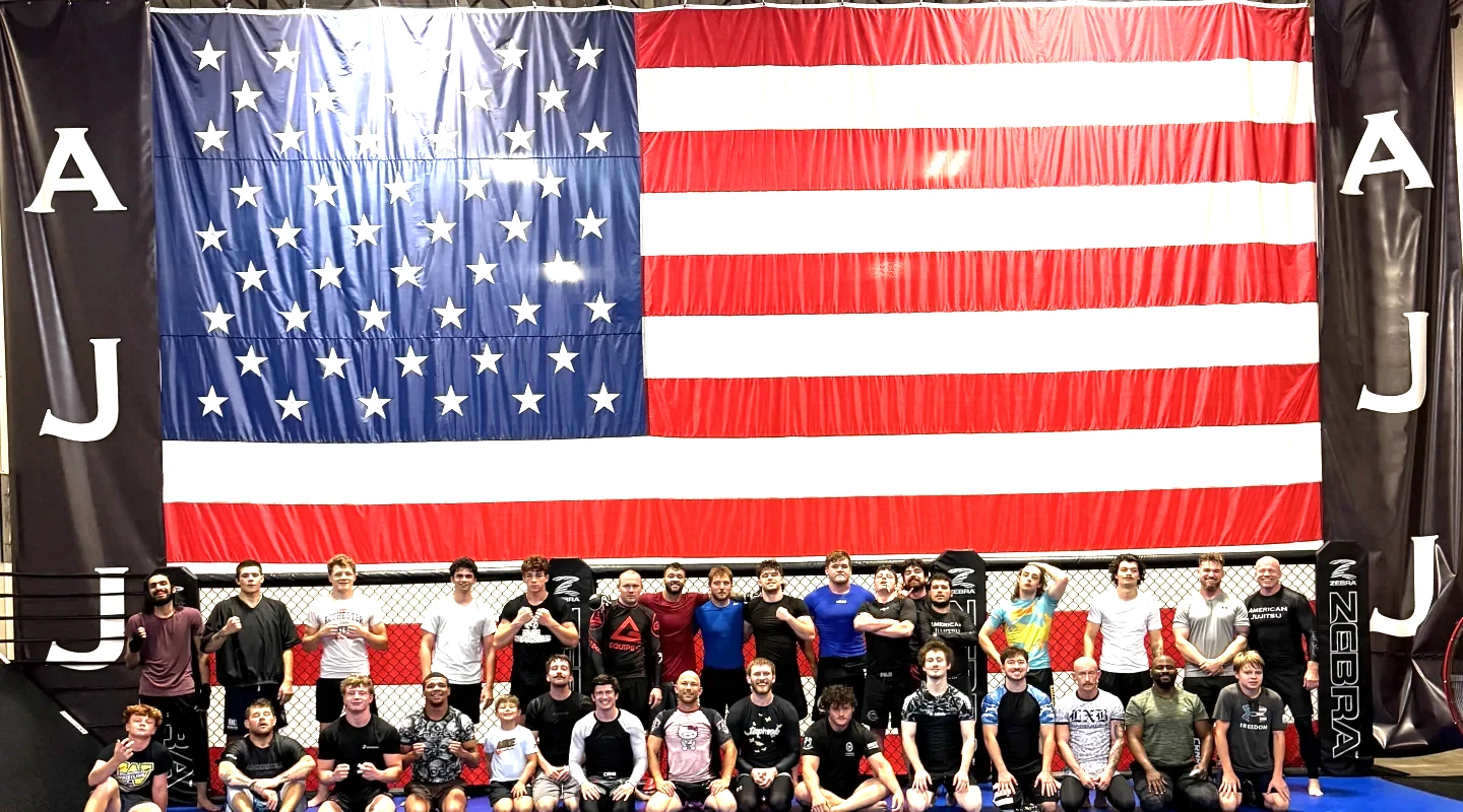 American Jujitsu team members posing together in front of a large American flag inside the gym in Springfield, IL