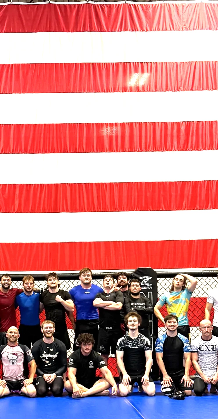 American Jujitsu team members posing together in front of a large American flag inside the gym in Springfield, IL