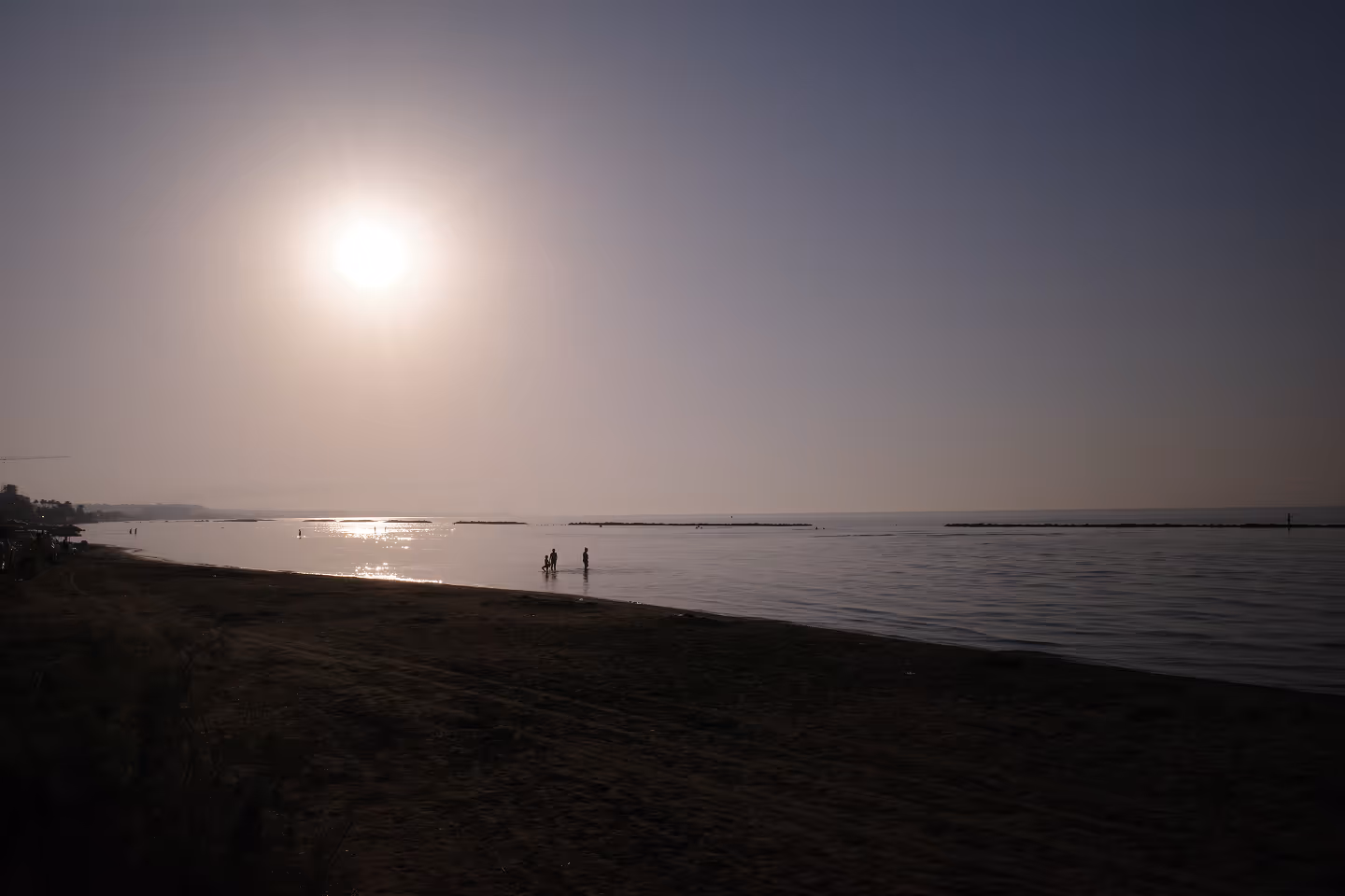 A beach scene at sunrise, with the sun low on the horizon casting a warm glow over the calm sea.