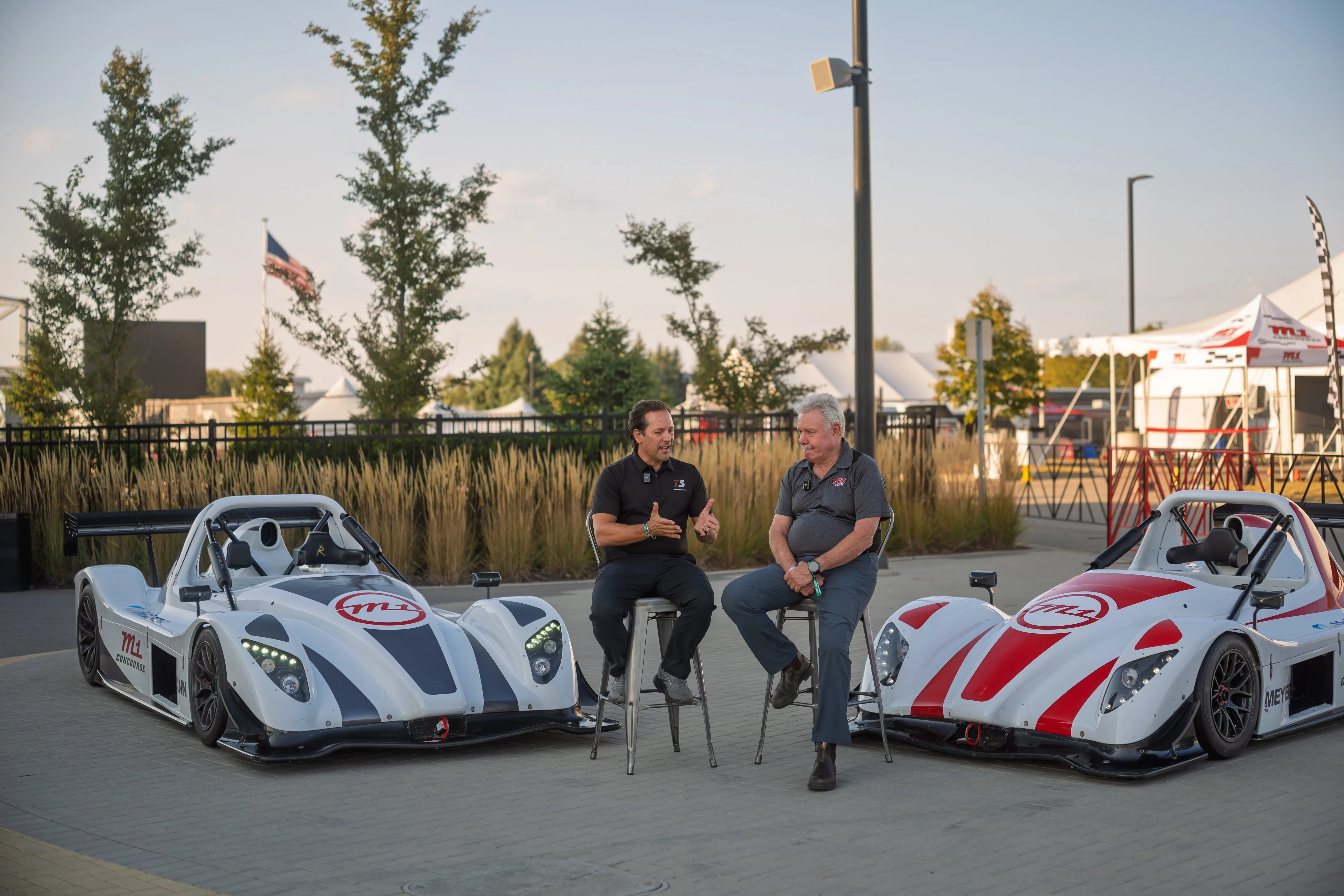 Francesco D’Avola from Team Stradle and Paul Zlotoff, owner of M1 Concourse, sit on high stools in front of two M1 Radicals to announce the partnership.