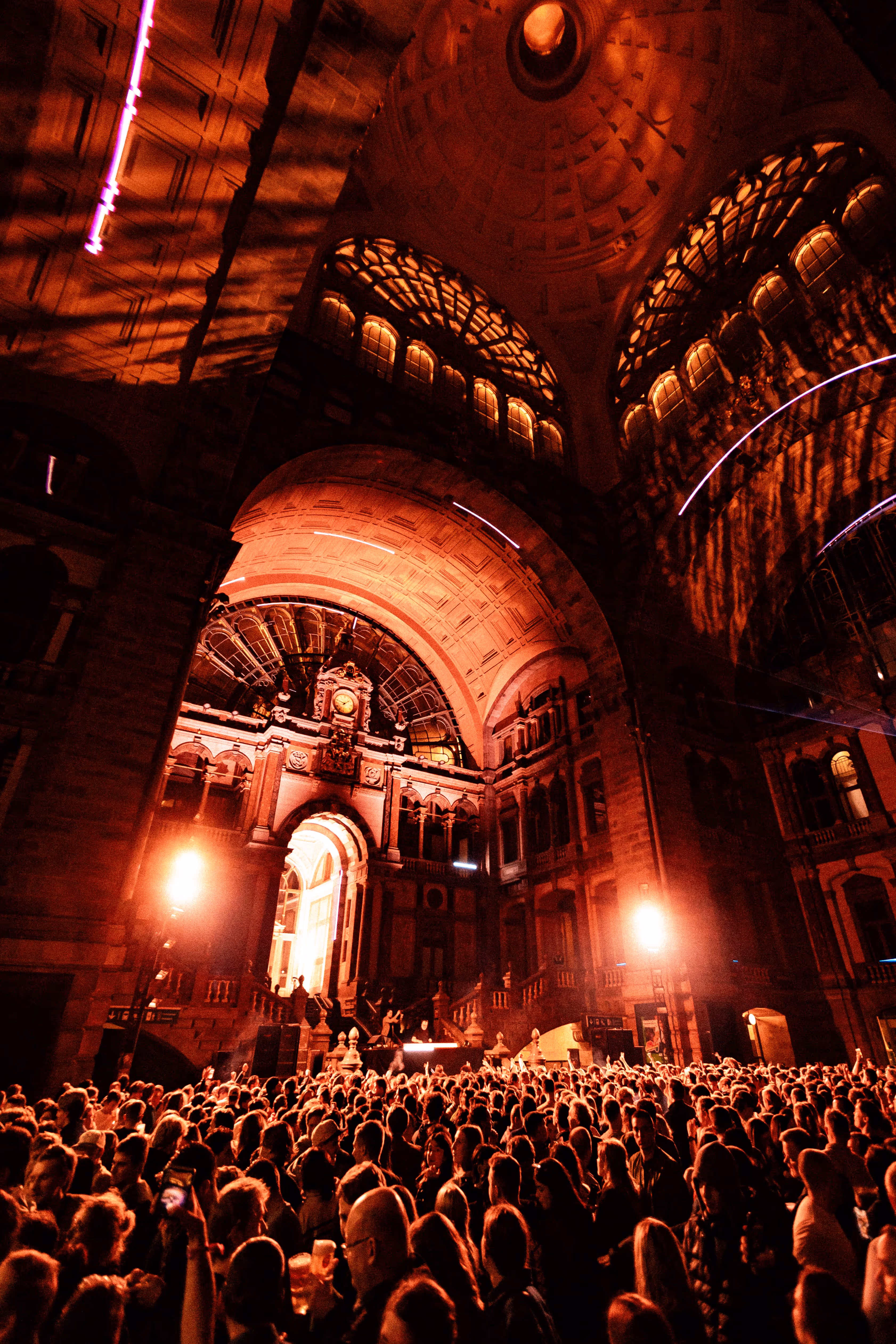Large crowd gathered inside an ornately arched building illuminated with warm orange lights during a nighttime event.