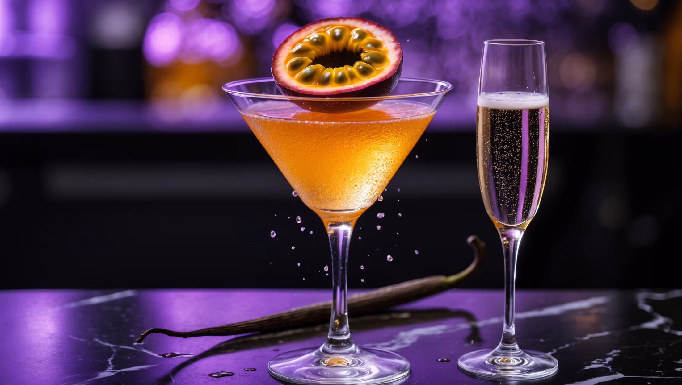 A crystal martini glass centered on a black marble bar top, filled with a vibrant golden-orange liquid that catches the ambient bar lighting with a subtle shimmer. The cocktail is crowned with a perfect half of passion fruit, seeds glistening, floating atop the creamy froth created by vigorous shaking. Beside it sits an elegant champagne flute filled with bubbling Prosecco, illuminated from behind to highlight the effervescence. A fine vanilla pod leans against the glass edge, with droplets of condensation running down both vessels suggesting perfect temperature. The scene is completed with ambient purple-pink lighting that casts a sensual glow across the sophisticated presentation.