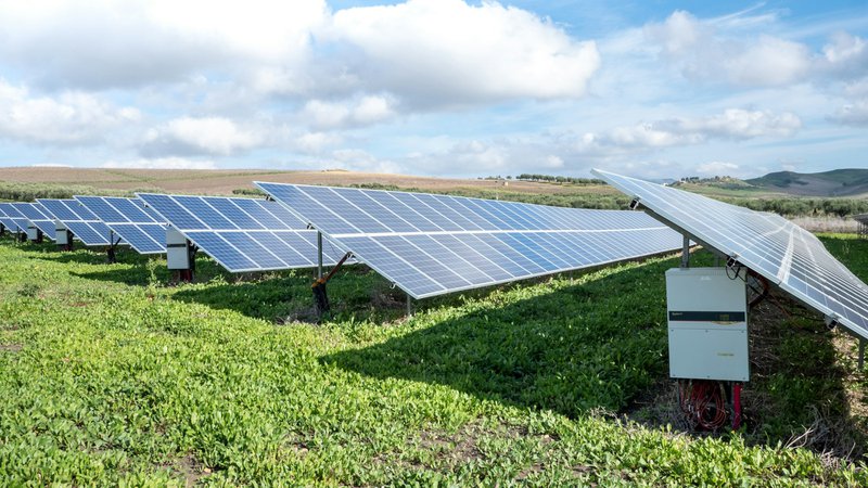 blue solar panels on green grass field under white clouds and blue sky during daytime that could help to mitigate environmental impact of ai by using more clean energy