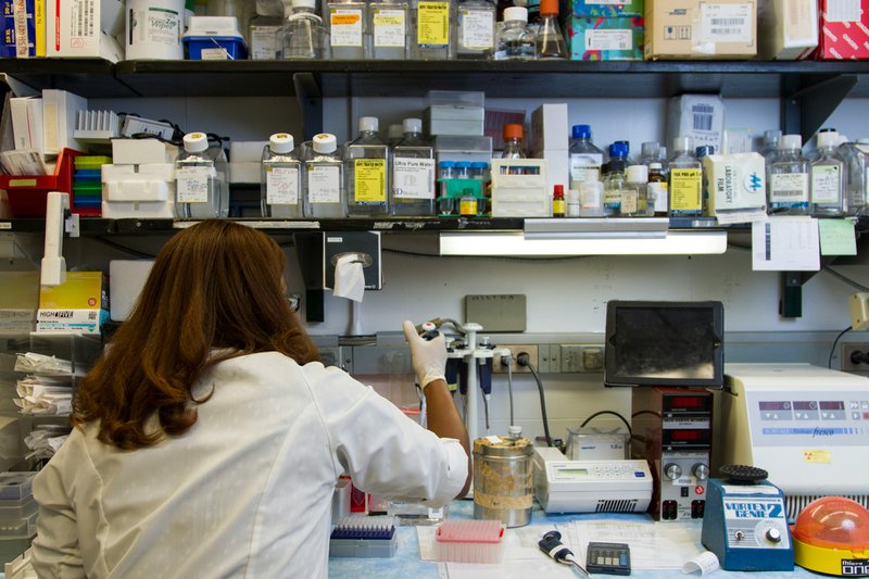 a woman scientist pipetting on work that might require research grant writing to fund