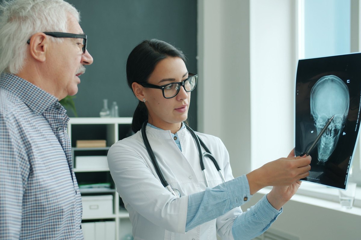 A doctor points to a skull X-ray as an older man listens beside her