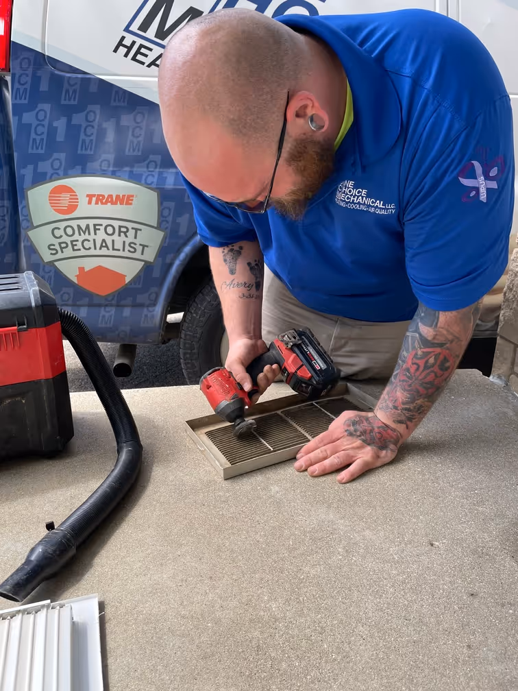 HVAC technician using drill to repair vent near Trane service van