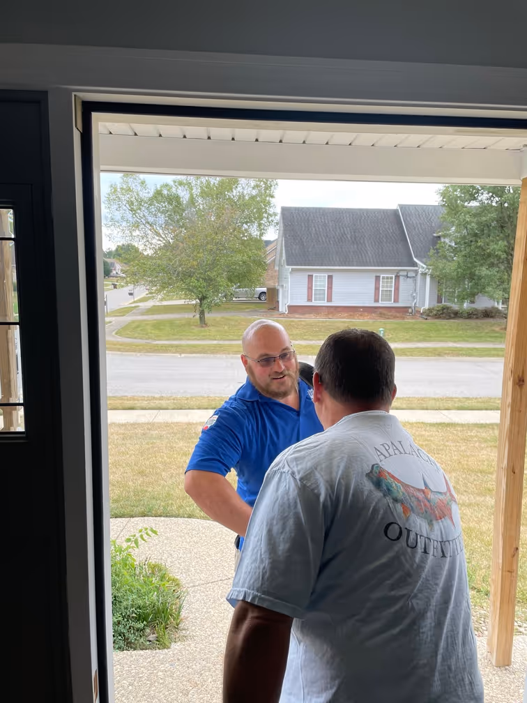 Two men talking at a front door with suburban house in background