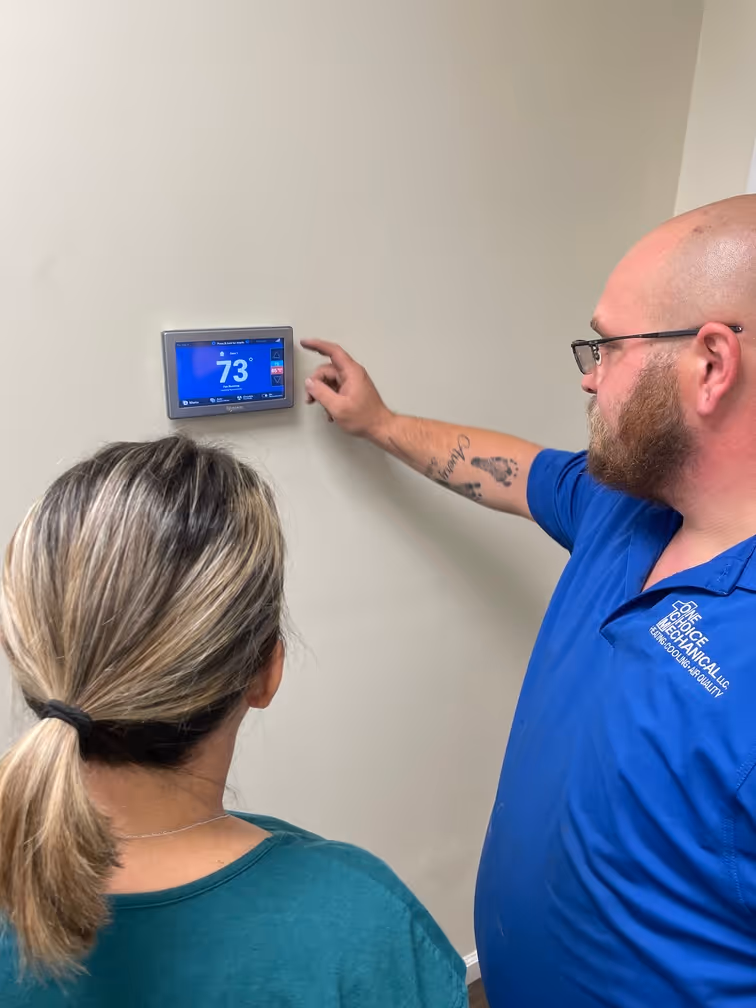 Technician adjusting digital thermostat to 73 degrees on wall