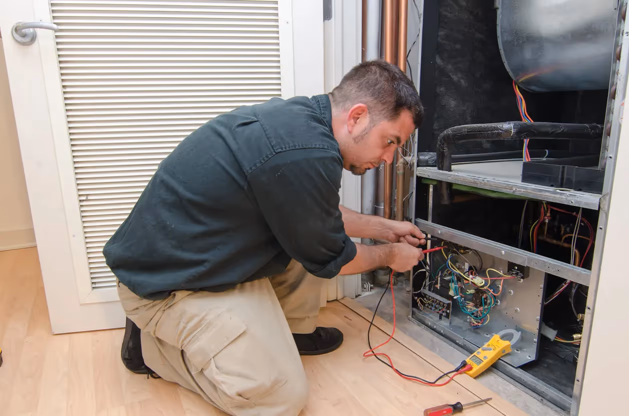 Technician performing electrical maintenance on HVAC system with multimeter