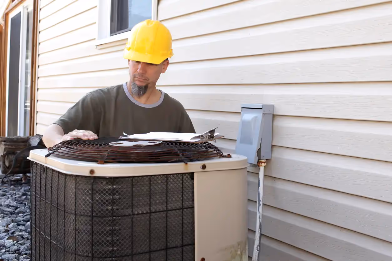 Worker in yellow hard hat inspects outdoor air conditioning unit