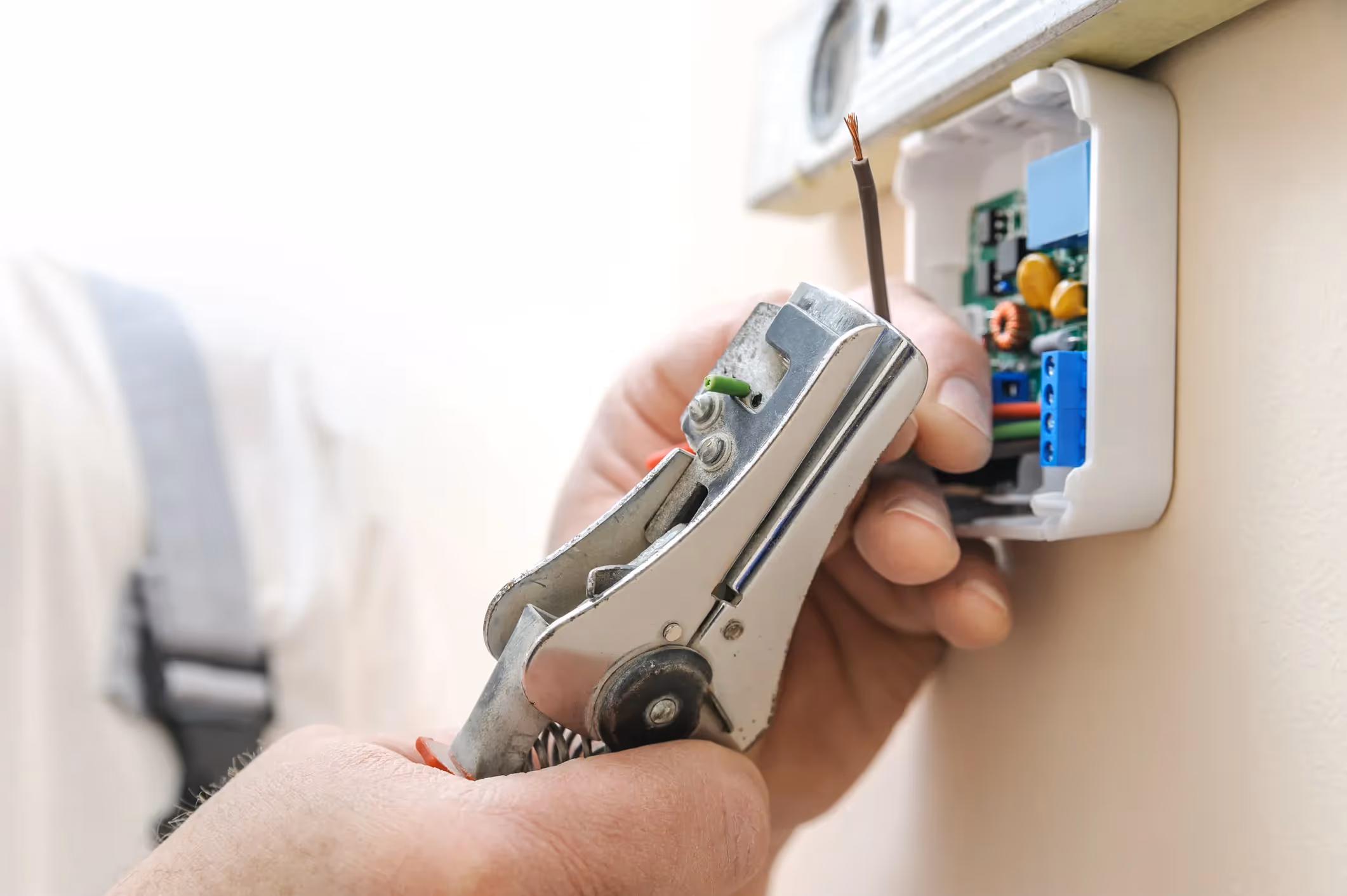 Electrician stripping wire with wire strippers near electrical outlet