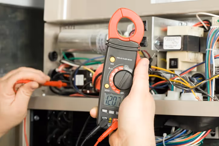 Electrician using clamp meter to measure voltage in electrical panel