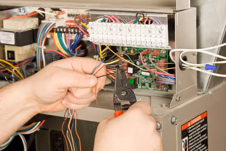 Electrician stripping and preparing wires inside an electrical control panel