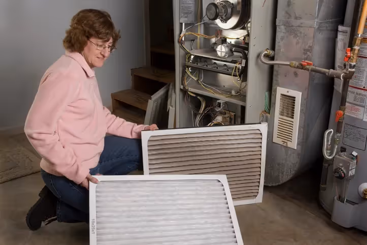Woman checking furnace filter in utility room with heating system