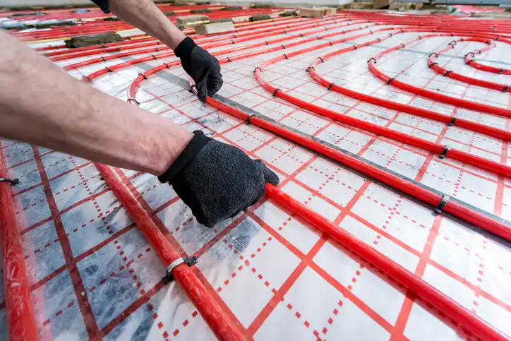 Worker installing red radiant floor heating pipes on insulation panel