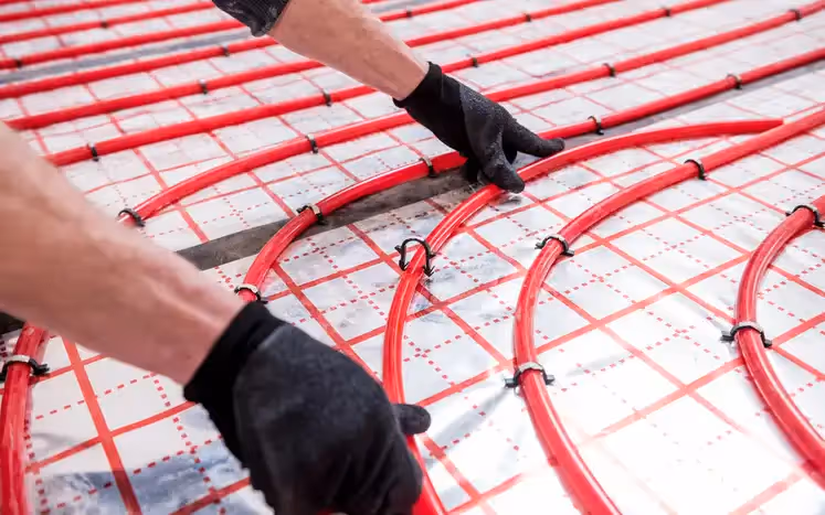 Hands installing red radiant floor heating pipes on white grid