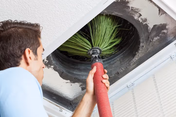 Person cleaning air vent with brush attachment in ceiling