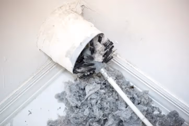 Lint-covered dryer vent brush cleaning out accumulated gray dryer lint