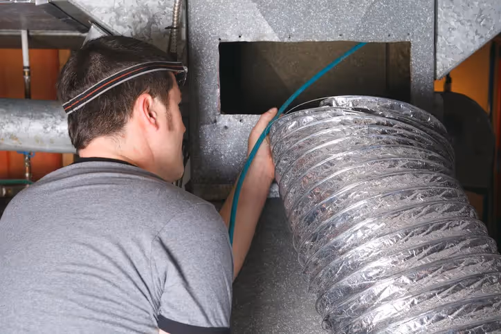Technician inspecting large metallic ventilation duct in industrial setting