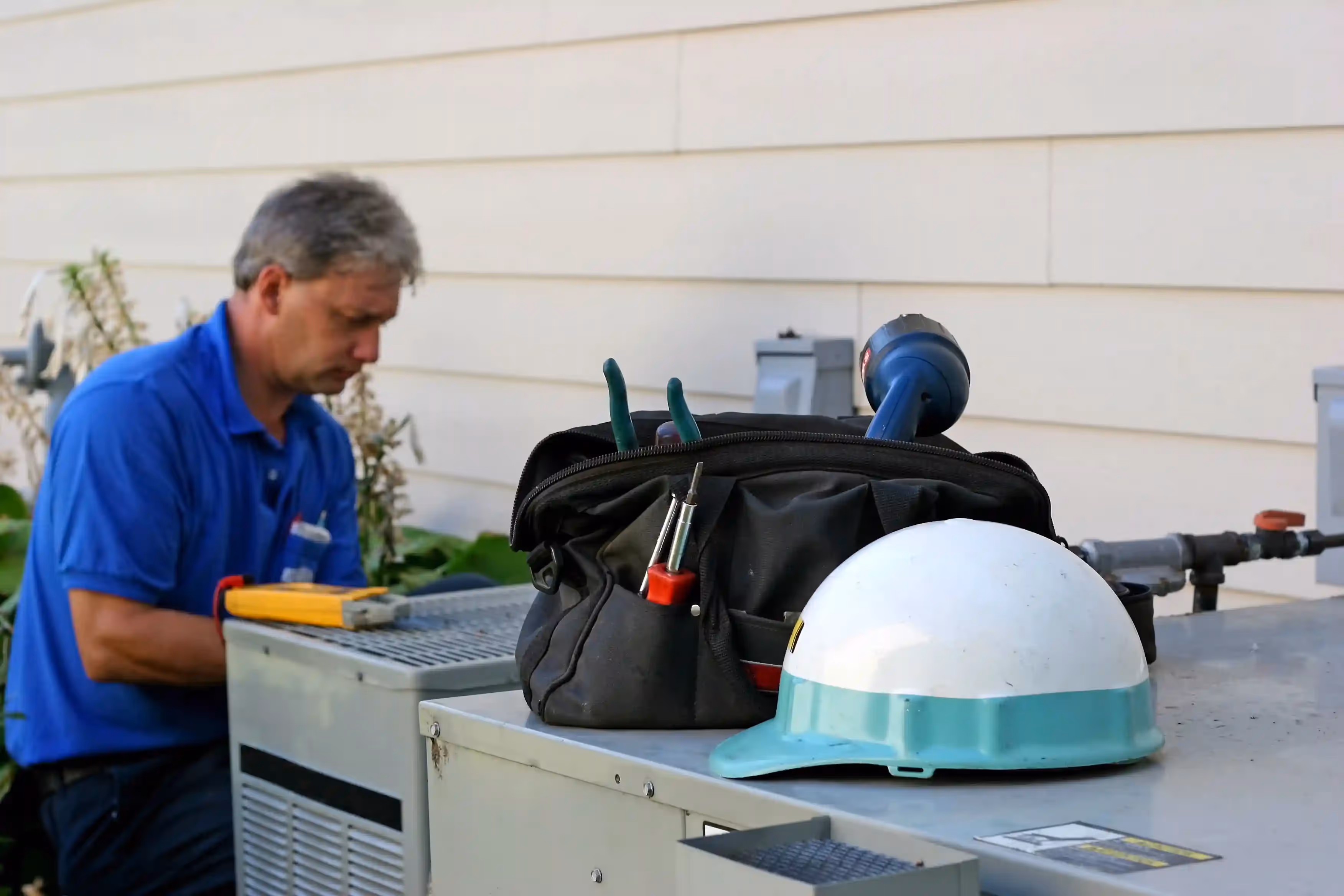 Worker with tools and safety helmet near industrial equipment outdoors