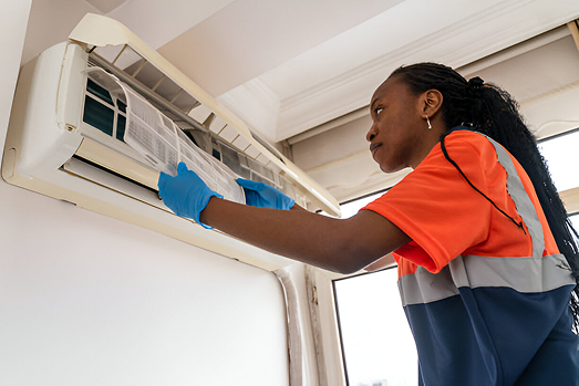 Technician in safety vest cleaning wall-mounted air conditioning unit