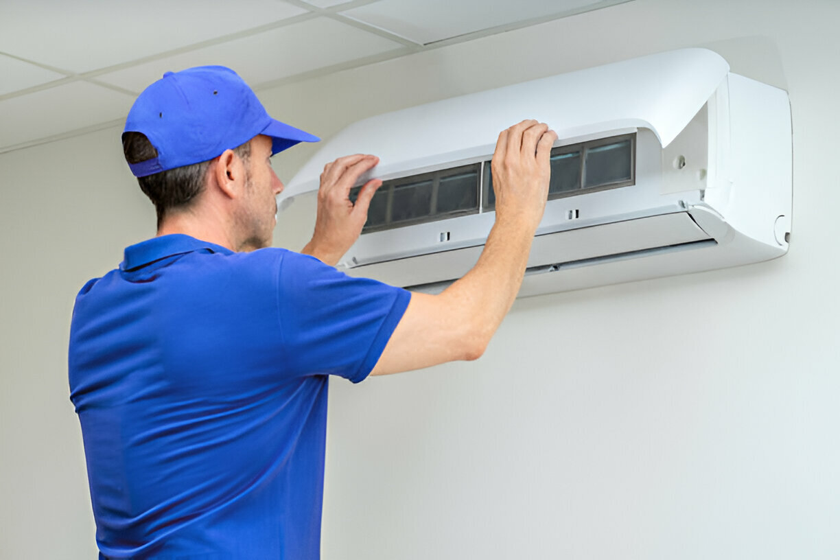 Technician in blue fixing air conditioning unit on white wall