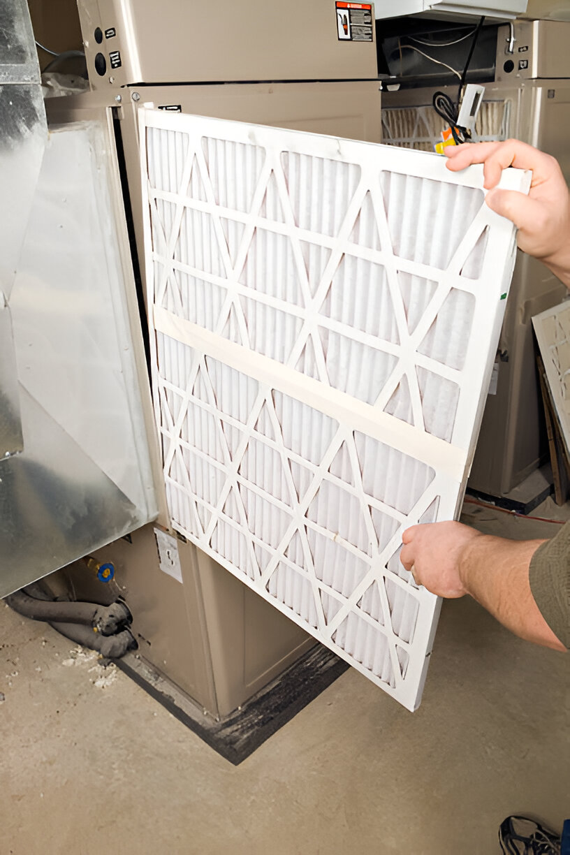Hands replacing a clean white air filter in an HVAC system