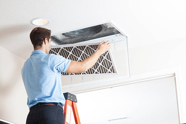 Technician replacing air filter in ceiling HVAC vent on ladder