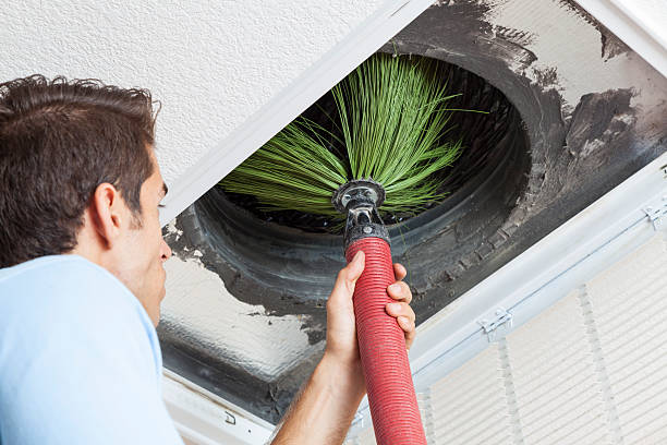 Person cleaning air vent with green brush attachment on red handle