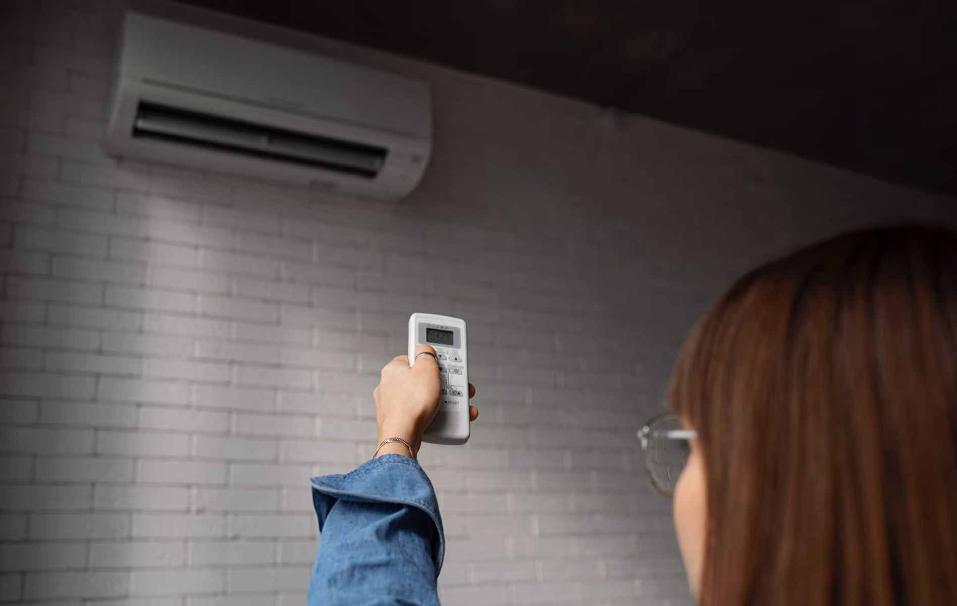 Person adjusting air conditioning remote control near wall-mounted unit